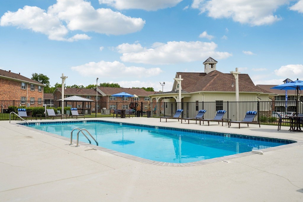 Outdoor swimming pool with lounge chairs and blue umbrellas at an apartment complex.