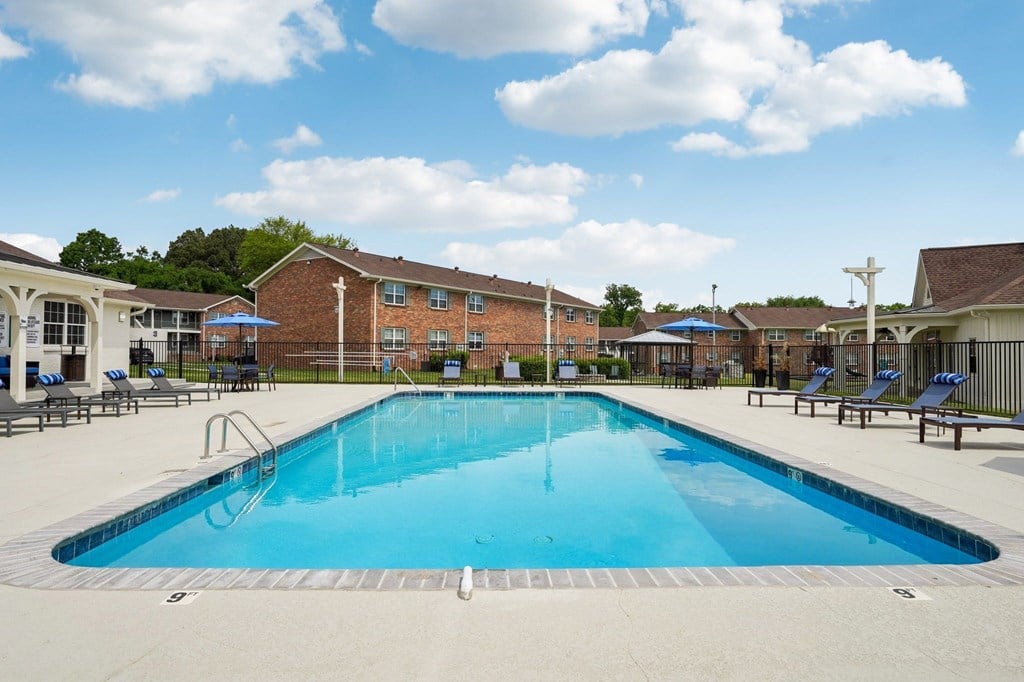 Apartment complex swimming pool with lounge chairs and blue umbrellas.