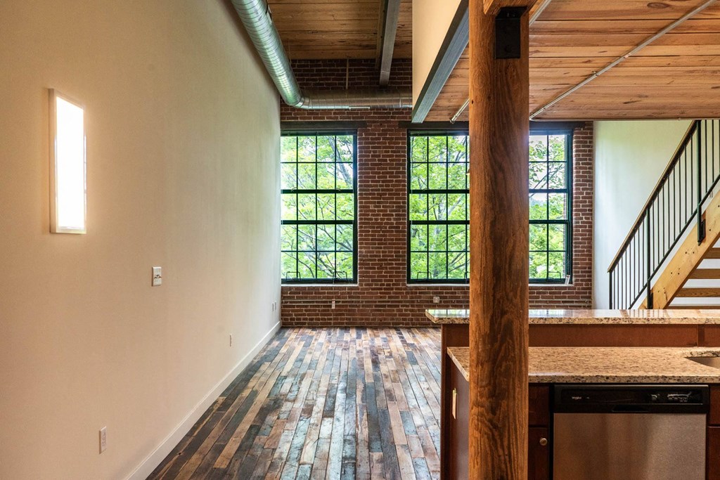 Modern kitchen and living space with exposed brick, hardwood floors, and large windows.