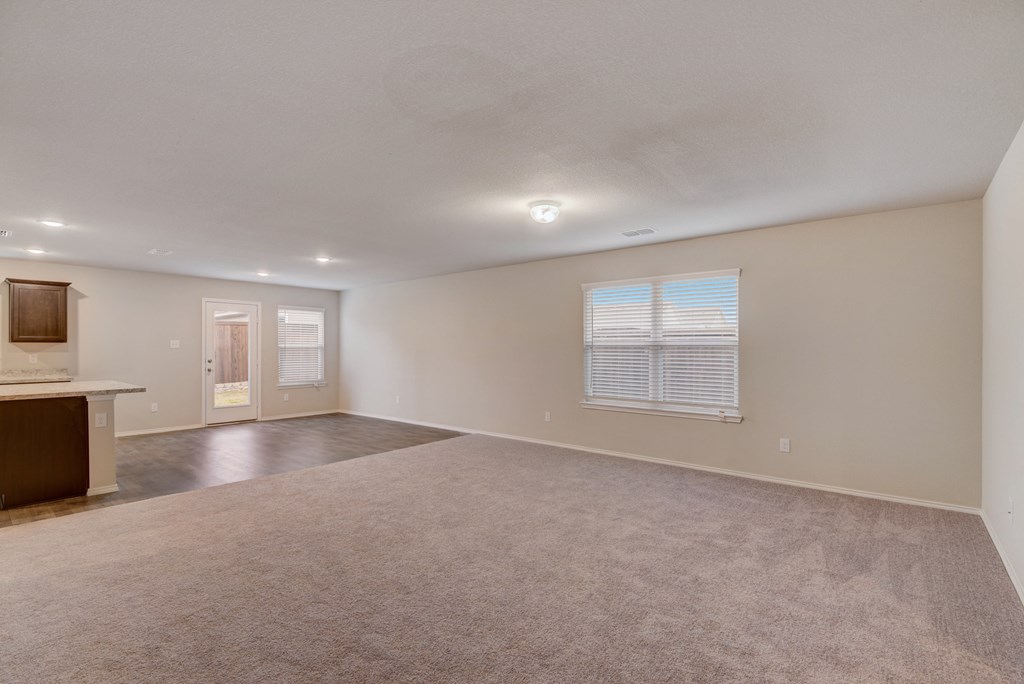 the living room and kitchen of an empty home with carpeting and a window