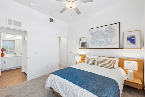 A bedroom with a bed, a ceiling fan, and a painting on the wall.
