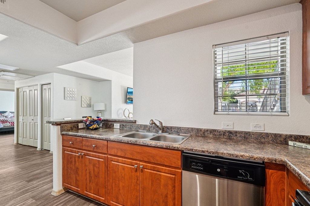 A kitchen with a stainless steel dishwasher and wooden cabinets.