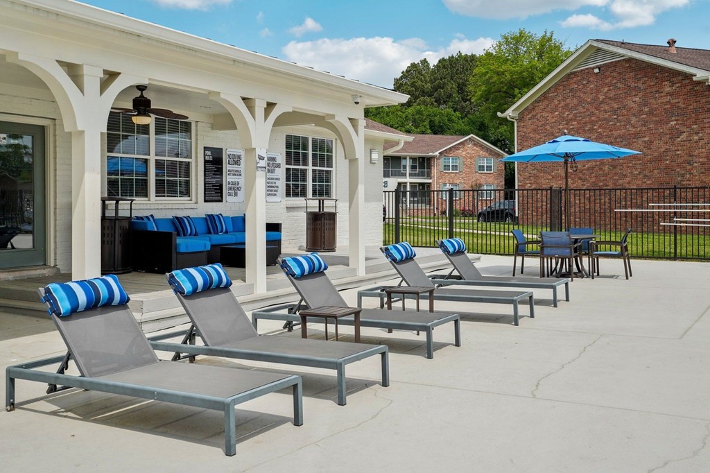 Apartment complex pool area with lounge chairs, patio furniture, and pool rules sign.