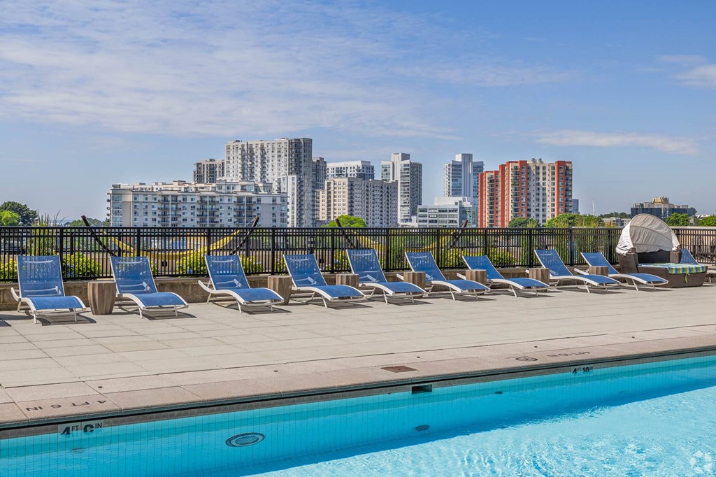 a row of lounge chairs next to a pool with a city in the background