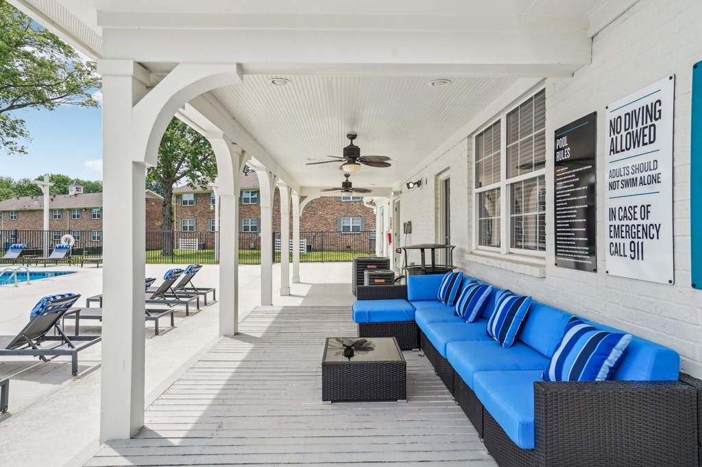 Poolside patio with blue cushioned seating, ceiling fans, and pool rules signage.