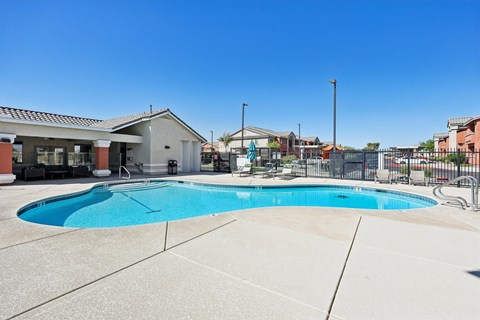 A large outdoor swimming pool surrounded by a concrete patio and a metal fence.