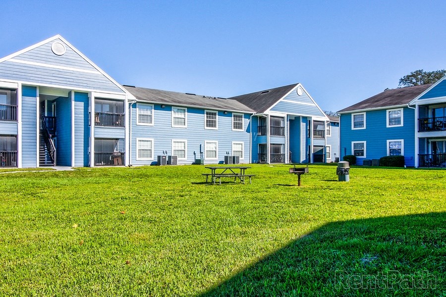 Open green area with picnic table and grill at The Commons apartment community in Tampa, Florida.