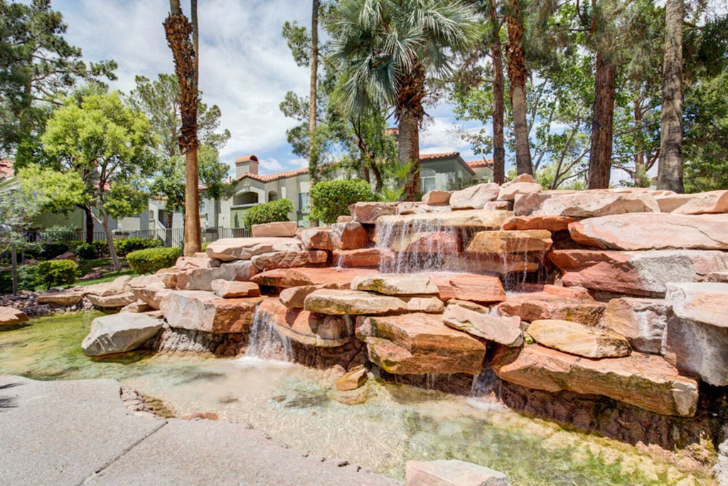 a waterfall in the backyard of a home with rocks and palm trees