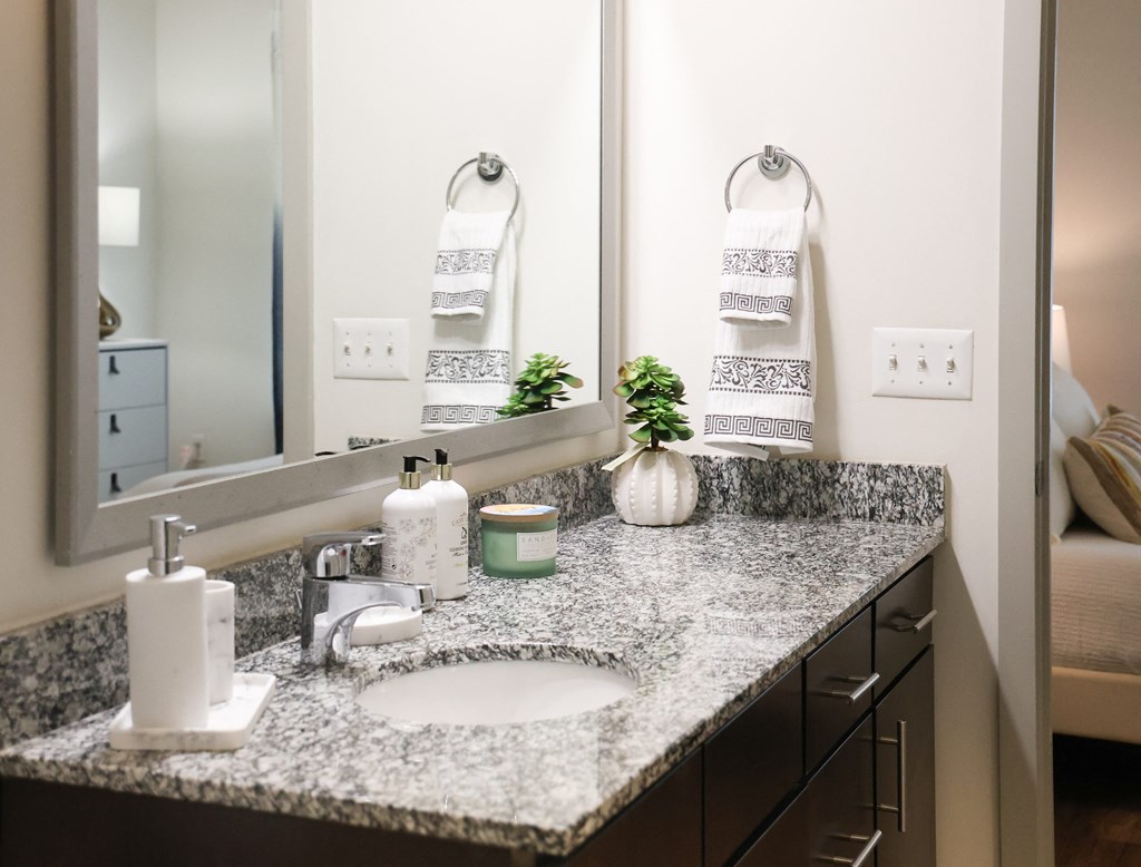 Modern bathroom with granite countertop, white sink, decorative towels, and toiletries.