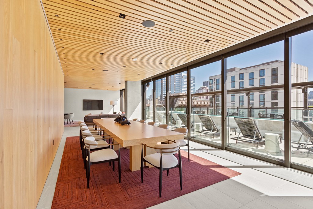 a long wooden table with white chairs on a red rug in a room with floor to ceiling