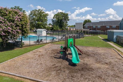 A playground with a green slide and a pool in the background.