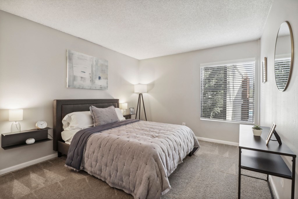 A bedroom with a bed, nightstand, and a window with blinds.