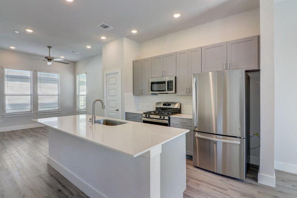 Pet Friendly Single Family Homes for Rent in Arlington TX - Mission on Ascension - Modern Kitchen with Stainless Steel Appliances, White Countertops, Grey Cabinetry, Tile Backsplash, Large Kitchen Island, Windows, a Dining Area, a Ceiling Fan, and Contemporary Tile and Wood-Engineered Plank Flooring