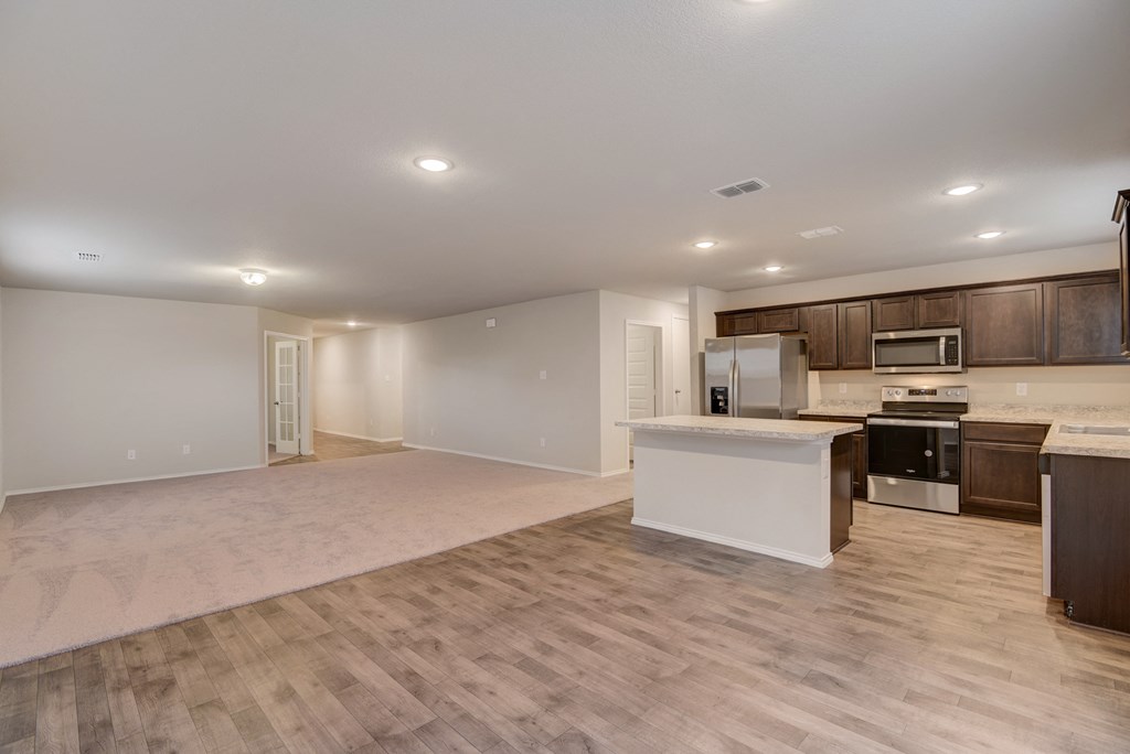 an empty living room with a kitchen with a microwave and a sink