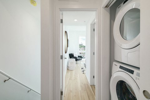 A white washing machine is in the foreground of a hallway.