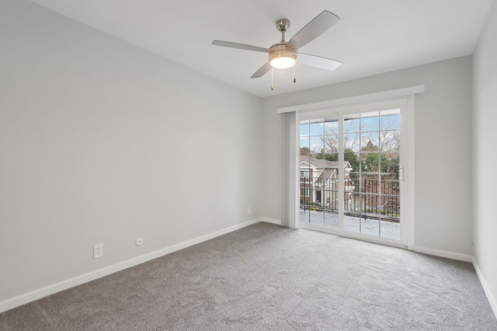 A room with a ceiling fan and a sliding glass door leading to a balcony.