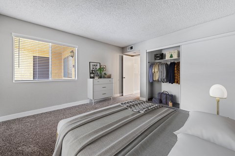 Colton, CA, Apartments Near Loma Linda University Medical Center - Ardella at Reche Canyon - Bedroom Features A Bed With Neutral Bedding, Plush Carpet, A Large Window With Blinds, And A Dresser.
