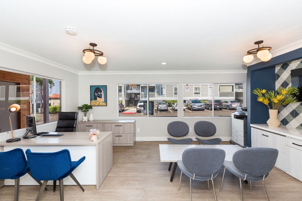 a living room with blue chairs and a white desk and a window