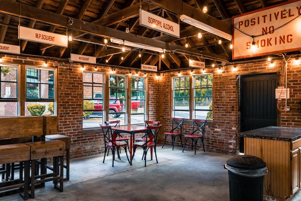 Interior of a brick pavilion with tables, chairs, and hanging signs for solvents and "Positively No Smoking".