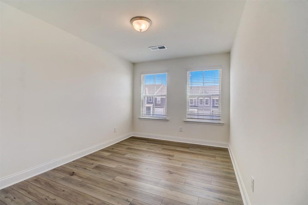 a bedroom with hardwood floors and two windows