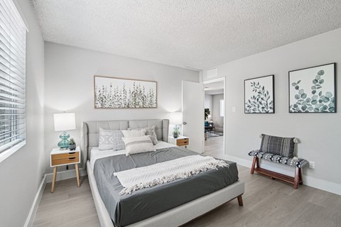 One-Bedroom Apartments in North Mountain Village, Phoenix, AZ - Ardella on 28th - Spacious Bedroom With Upholstered Bed, Side Tables, Lamps, Soft Gray Bedding, Bed Bench, and Large Window With Blinds.