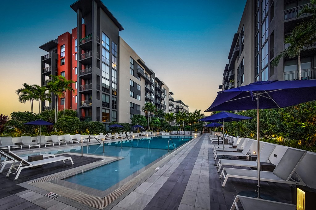 a swimming pool with chairs and umbrellas in front of some tall buildings
