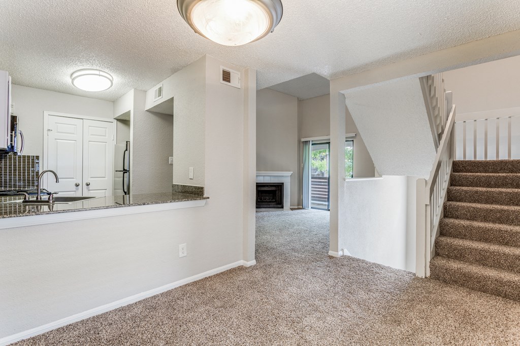 a living room with a staircase and a kitchen in the background