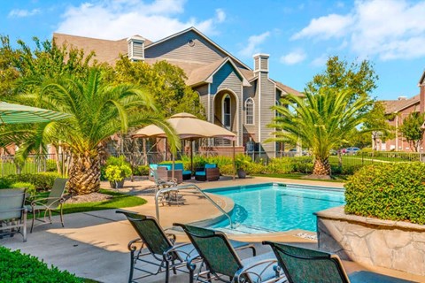 a swimming pool with chairs and umbrellas in front of a house