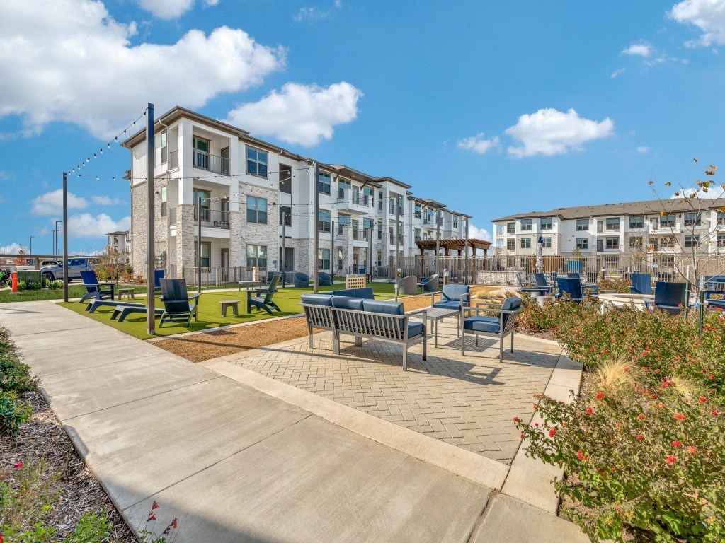 an outdoor seating area with benches and picnic tables in front of an apartment building