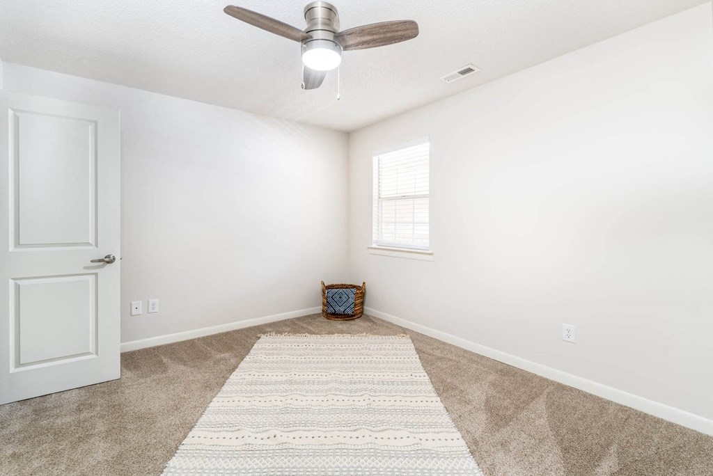 an empty living room with a ceiling fan and a rug