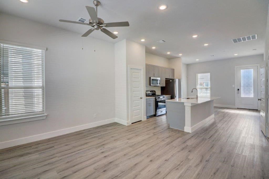 an empty living room with a kitchen and a ceiling fan