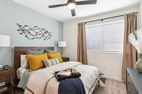 A bedroom with a bed, a ceiling fan, and a wall art.