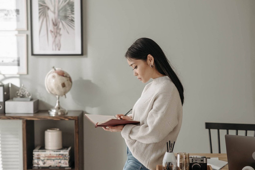 a woman standing in a living room writing in a notebook