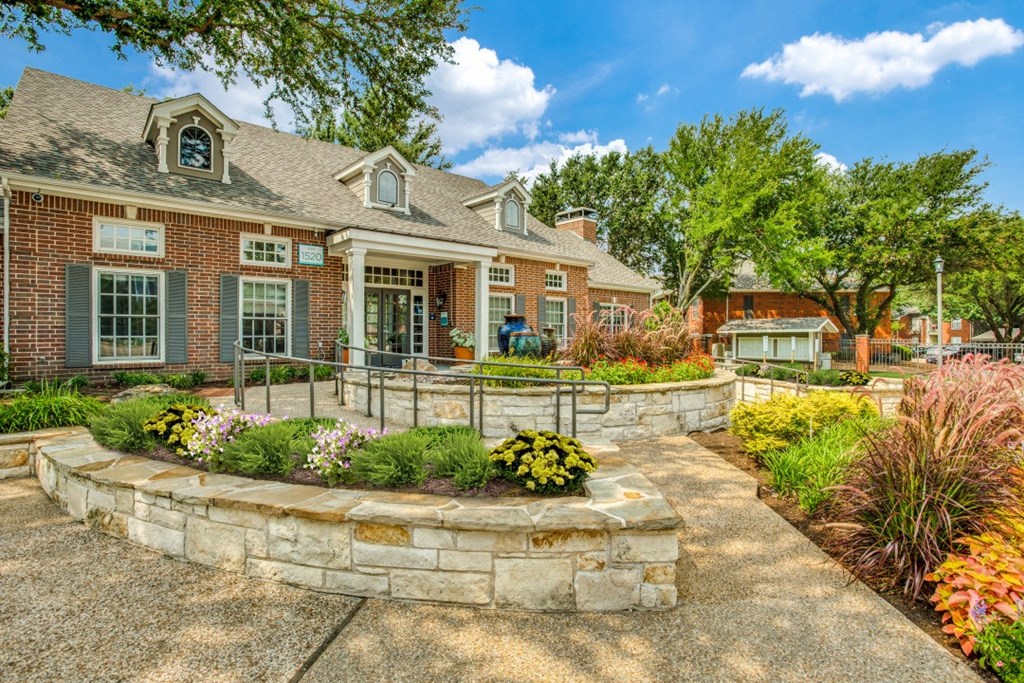 the front yard of a brick house with a stone retaining wall and landscaping