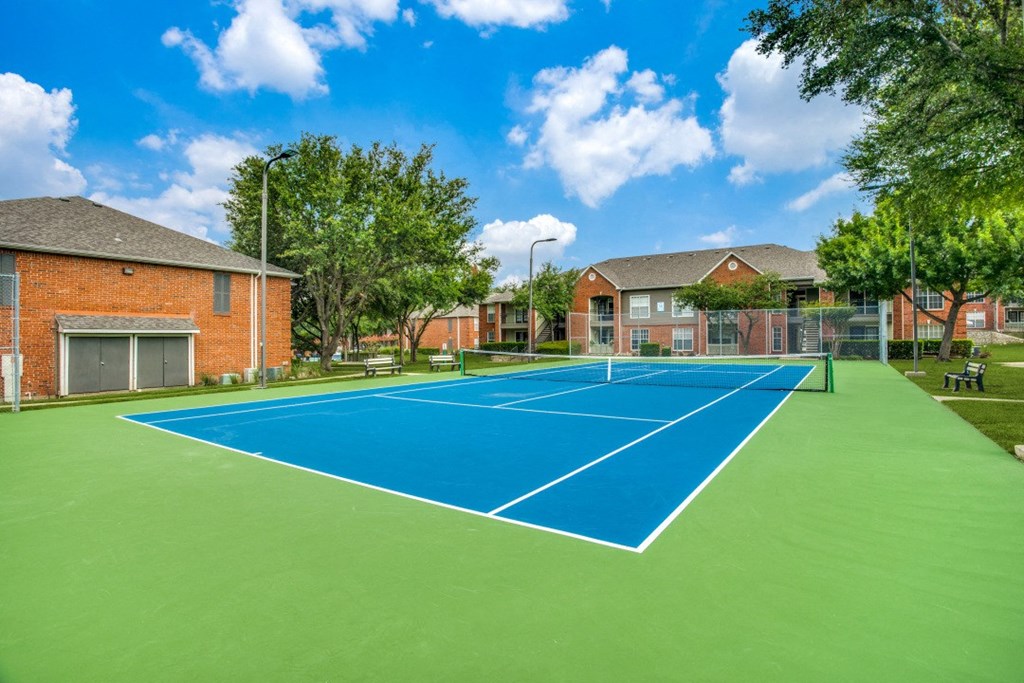 a tennis court in front of two houses with a blue and green tennis court