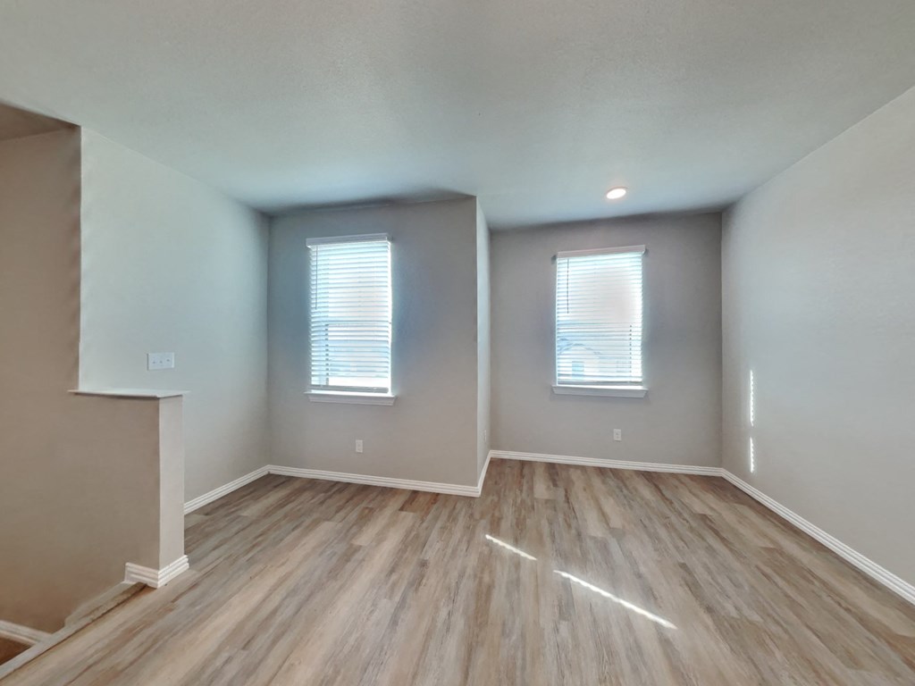 an empty living room with wood flooring and two windows