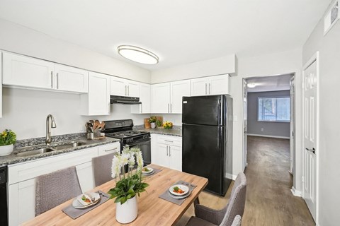 A black refrigerator sits in a kitchen with white cabinets and a wooden table.
