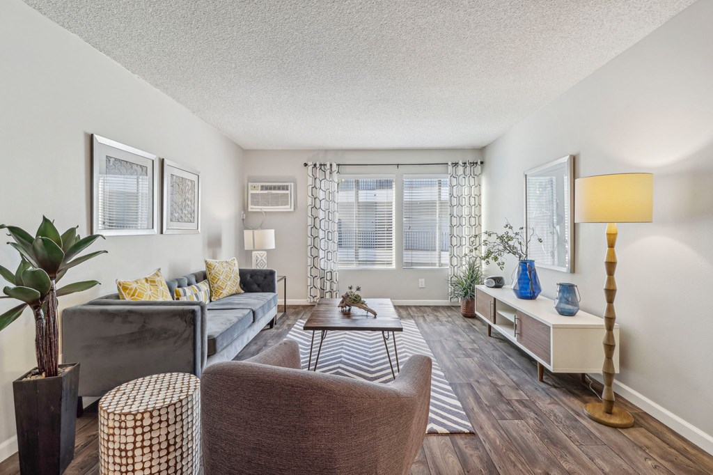 A living room with a grey couch, a brown chair, a wooden floor, and a large window.