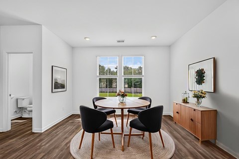 A dining room with a table set for two and a view of a green lawn and trees outside the window.