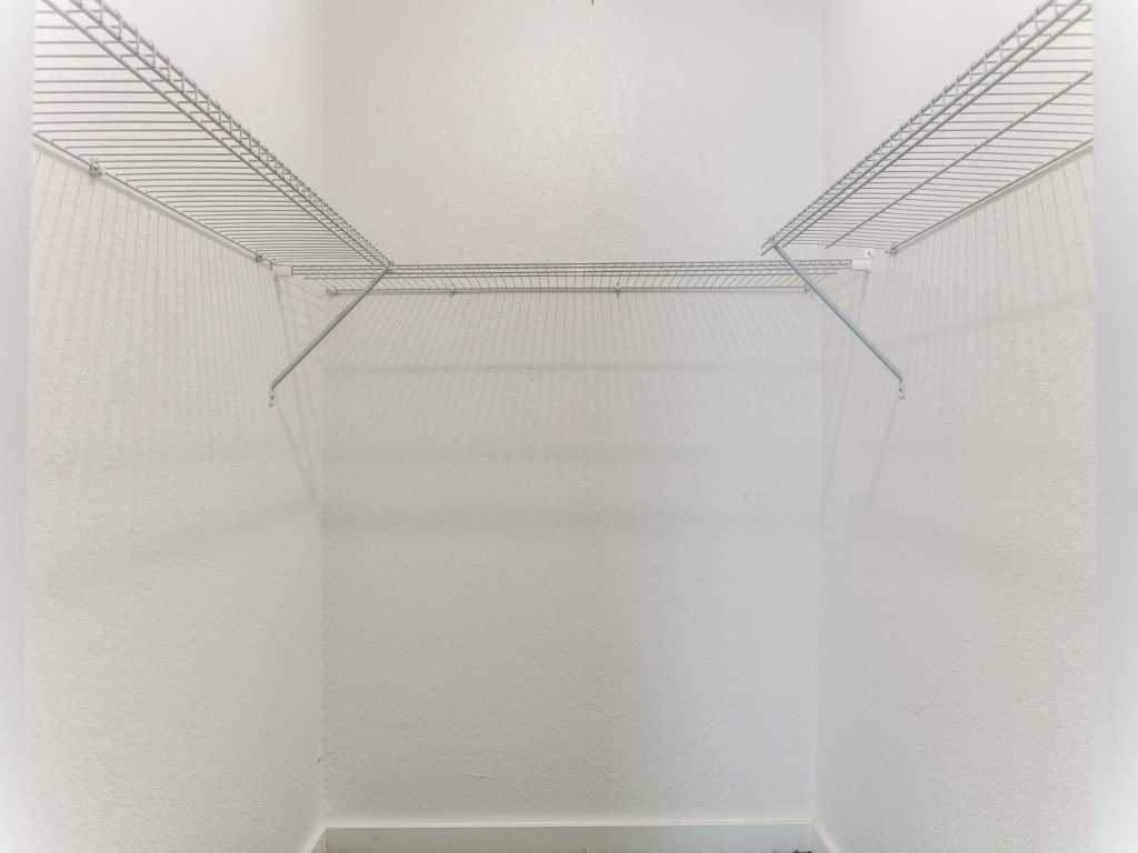 a walk in closet with white walls and a clear wire shelving system