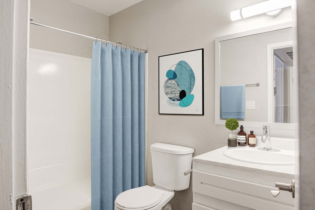 Two-Bedroom Apartments in Glendale, AZ - Spectra West - Bathroom with a Blue Shower Curtain, a White Shower and Bathtub, a Toilet, and a White Vanity