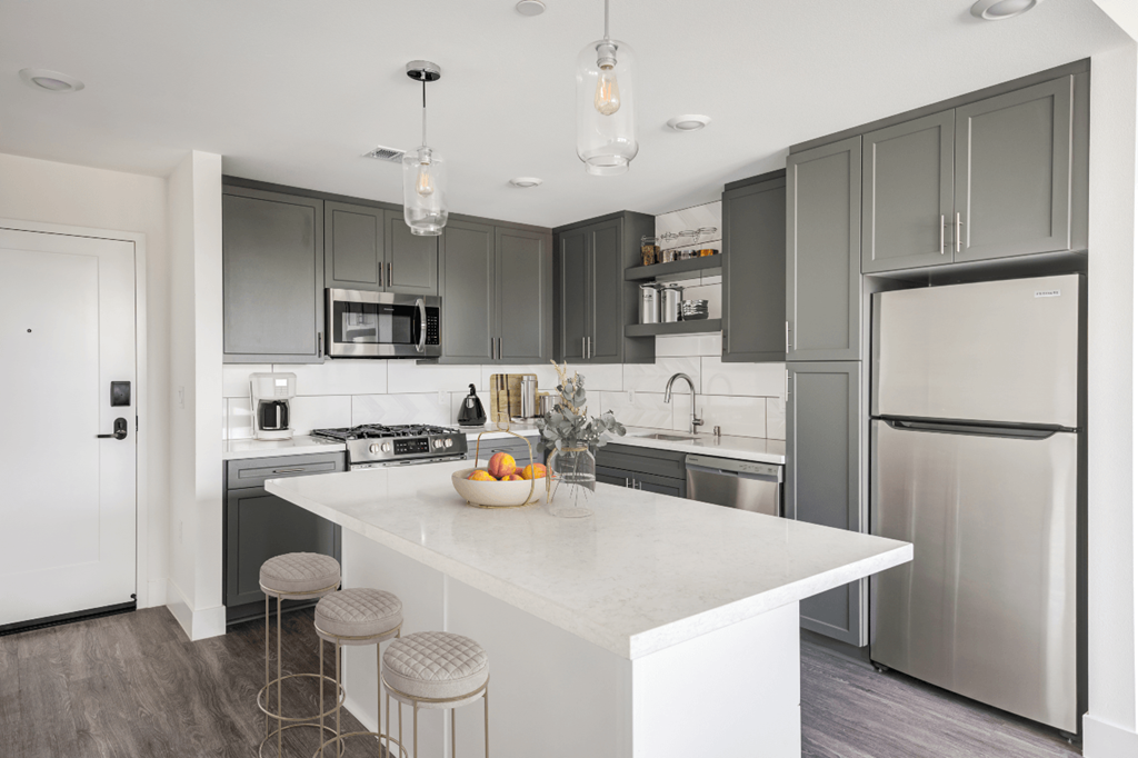 Apartments For Rent In Whitter, CA - Cierra - Kitchen With Vinyl Plank Flooring, Stainless Steel Appliance Package, Kitchen Island with Stool Seating, Quartz Countertops, And Grey Cabinets.