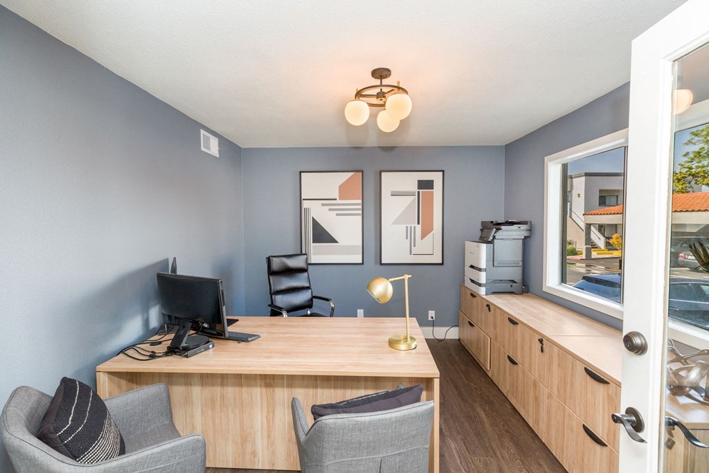 a desk with two chairs and a computer in a room with a window and a door