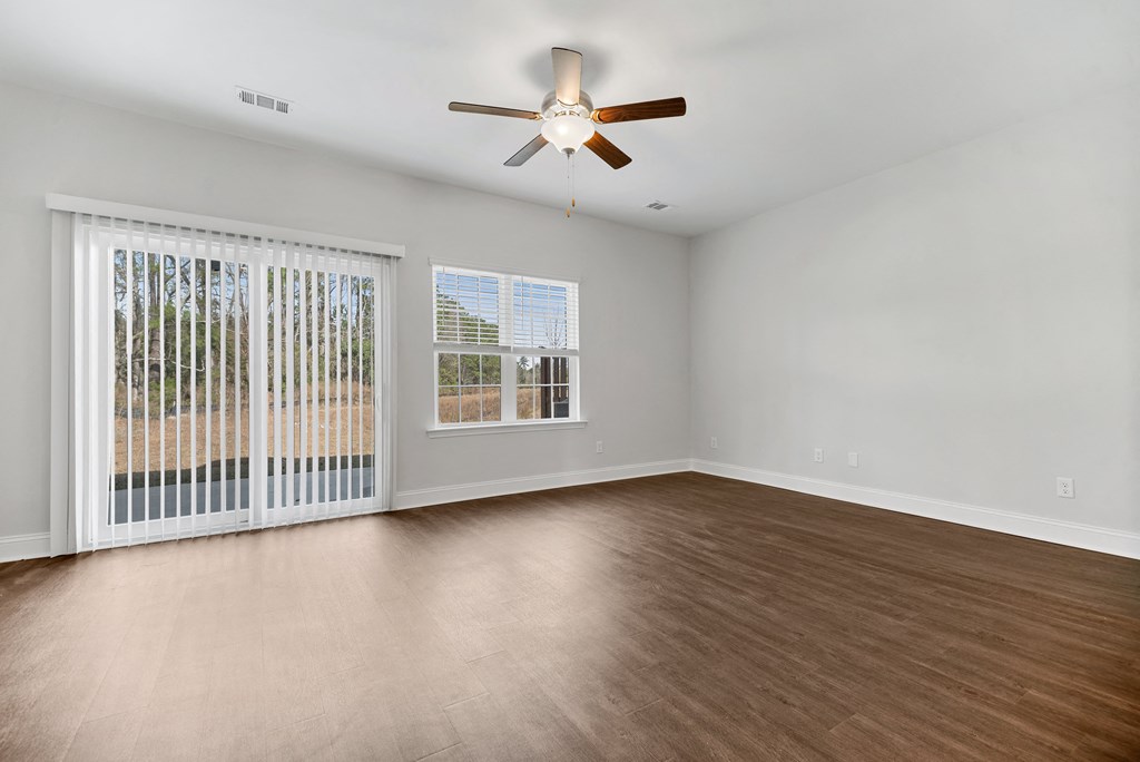 Cottonvale Towns in Savannah, GA photo of living room with large windows, ceiling fan, and hardwood flooring