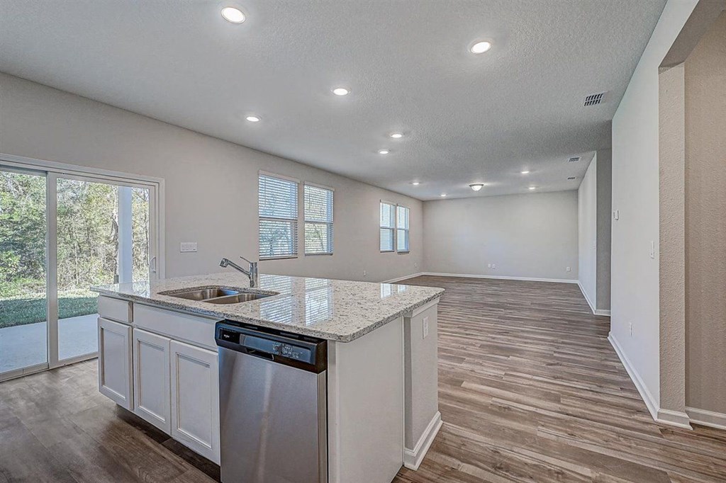 Open concept kitchen and living area with wood-look flooring, granite countertops, and stainless steel appliances.