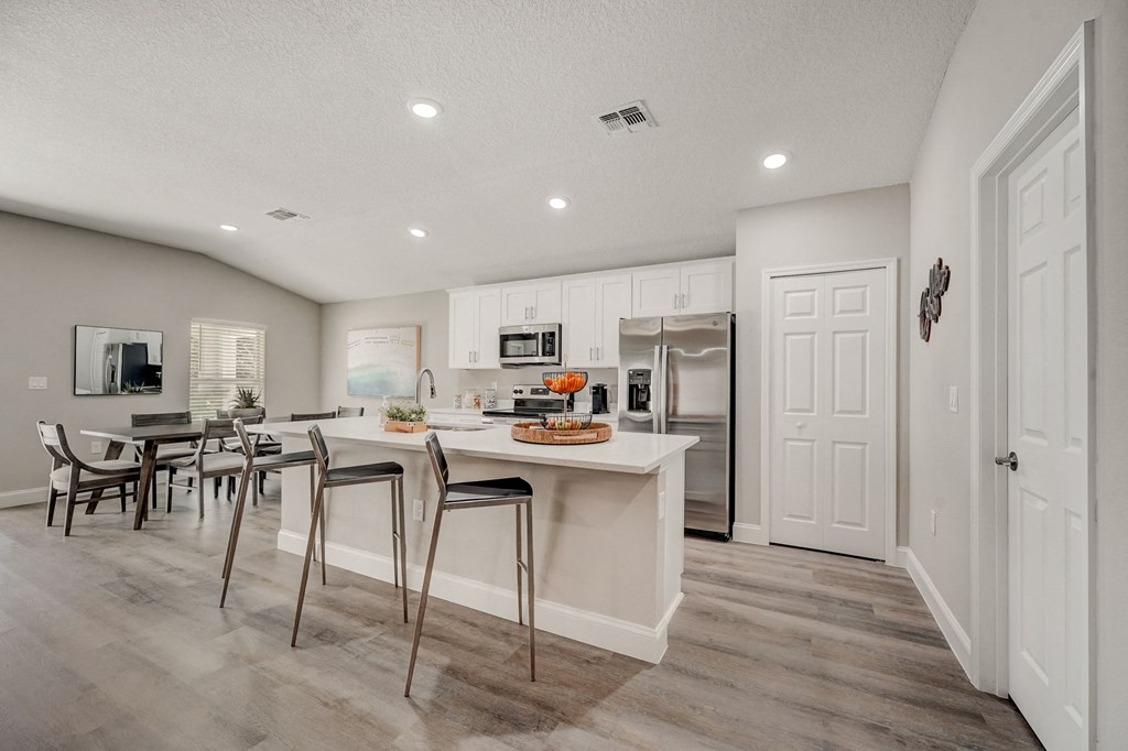 Luxury kitchen with an island and adjacent dining table with chairs at The Groves at Lake Ella in Lady Lake, Florida, a pet-friendly rental community.