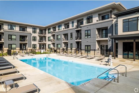 A swimming pool is surrounded by sun loungers in front of apartment buildings.