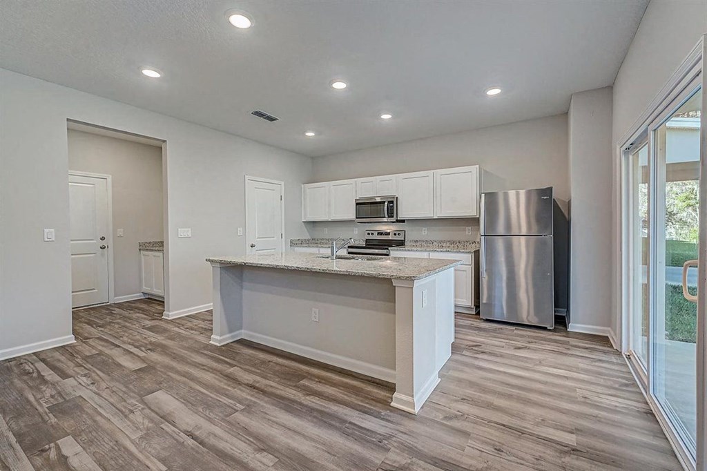 Modern kitchen with white cabinets, granite countertops, stainless steel appliances, and wood-look flooring.