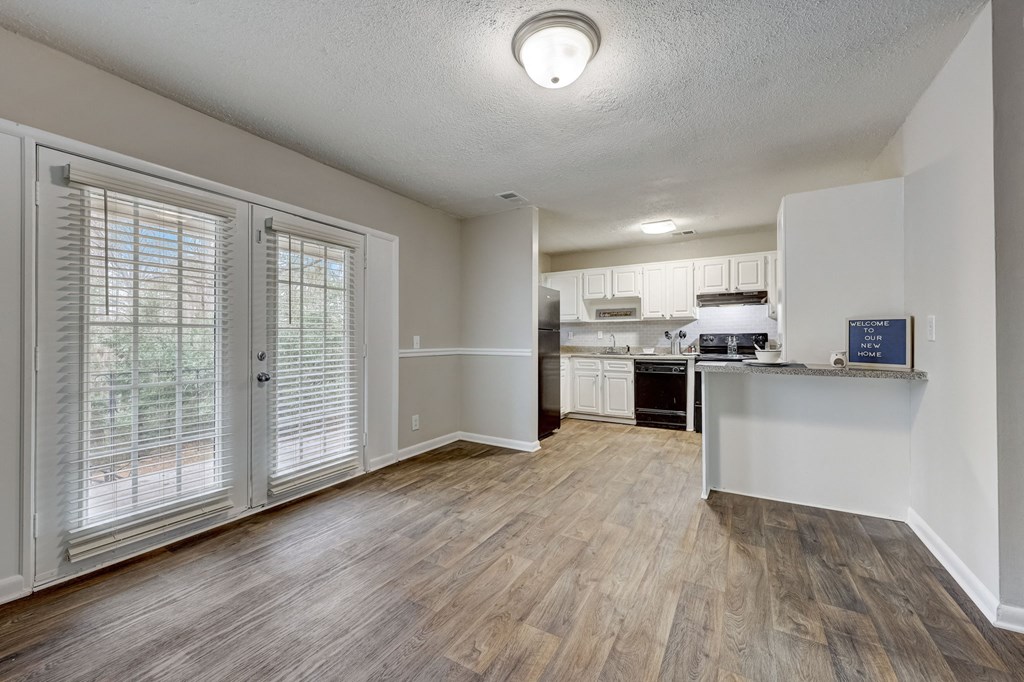 Apartments In Sandy Springs, GA for Rent – Celebration at Sandy Springs - the living room and kitchen of an apartment with white walls and wood floors