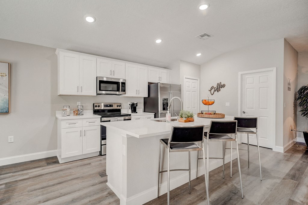 Luxury open kitchen with a large island and three stools at The Groves at Lake Ella in Lady Lake, Florida, a pet-friendly rental community.